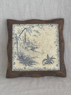 Antique French blue transferware tile trivet in a shaped wooden frame, showing a mosque, minaret and palm trees on a heavily crazed cream ground