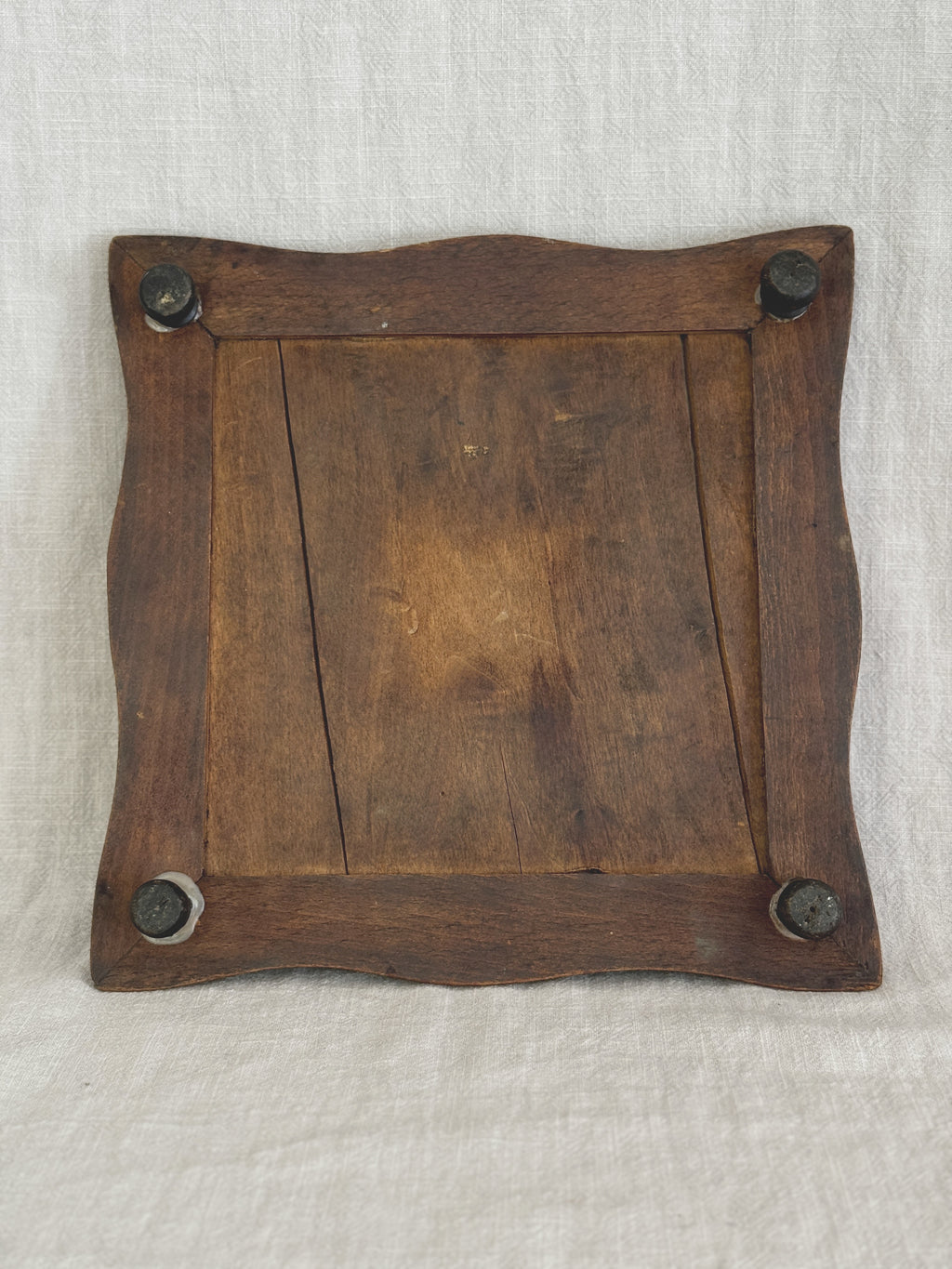 Underside of the wooden trivet frame, showing the plank back and four dark turned bun feet