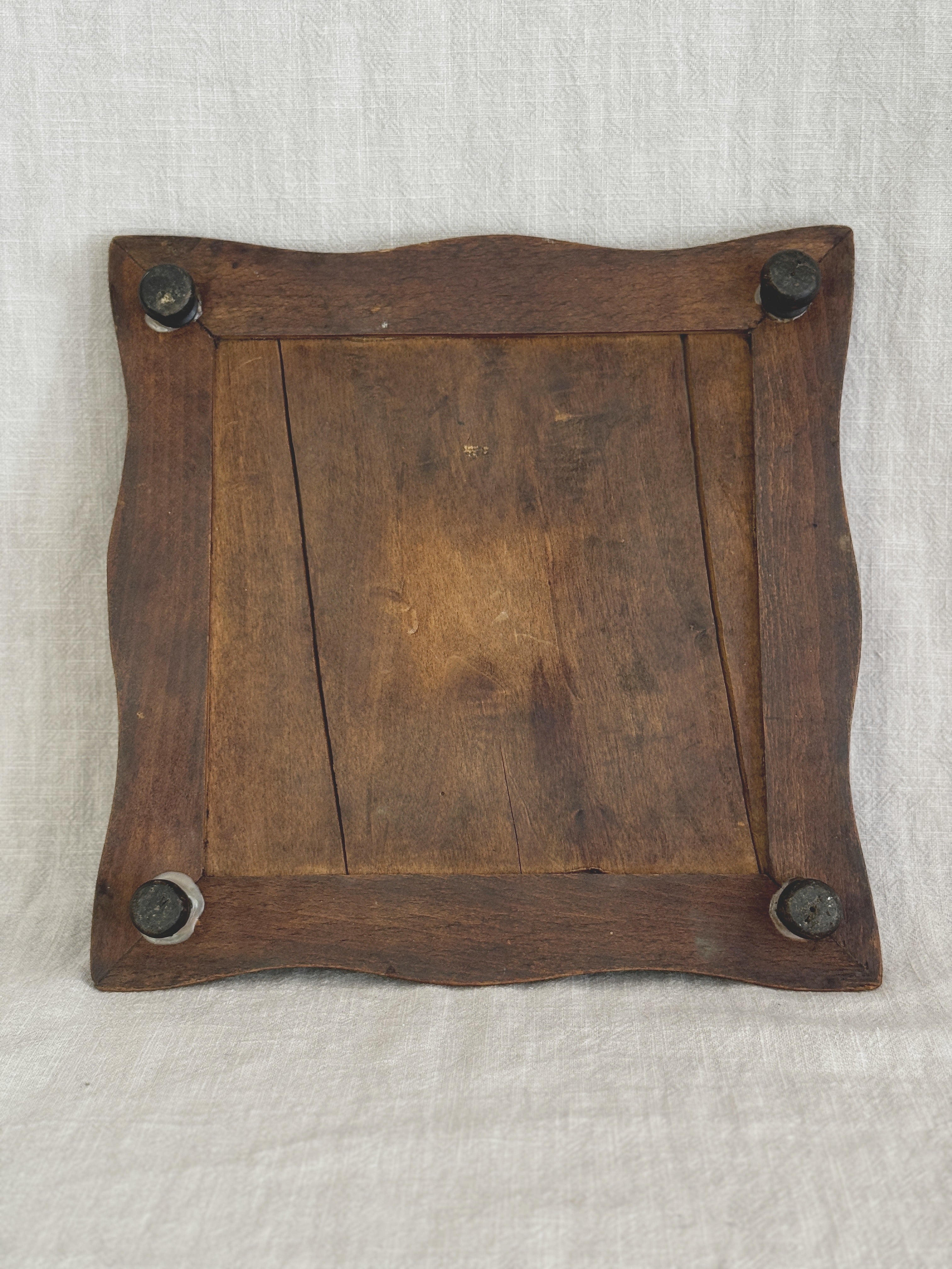 Underside of the wooden trivet frame, showing the plank back and four dark turned bun feet