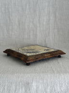 Side view of the framed French tile trivet, showing its low profile and small turned wooden feet