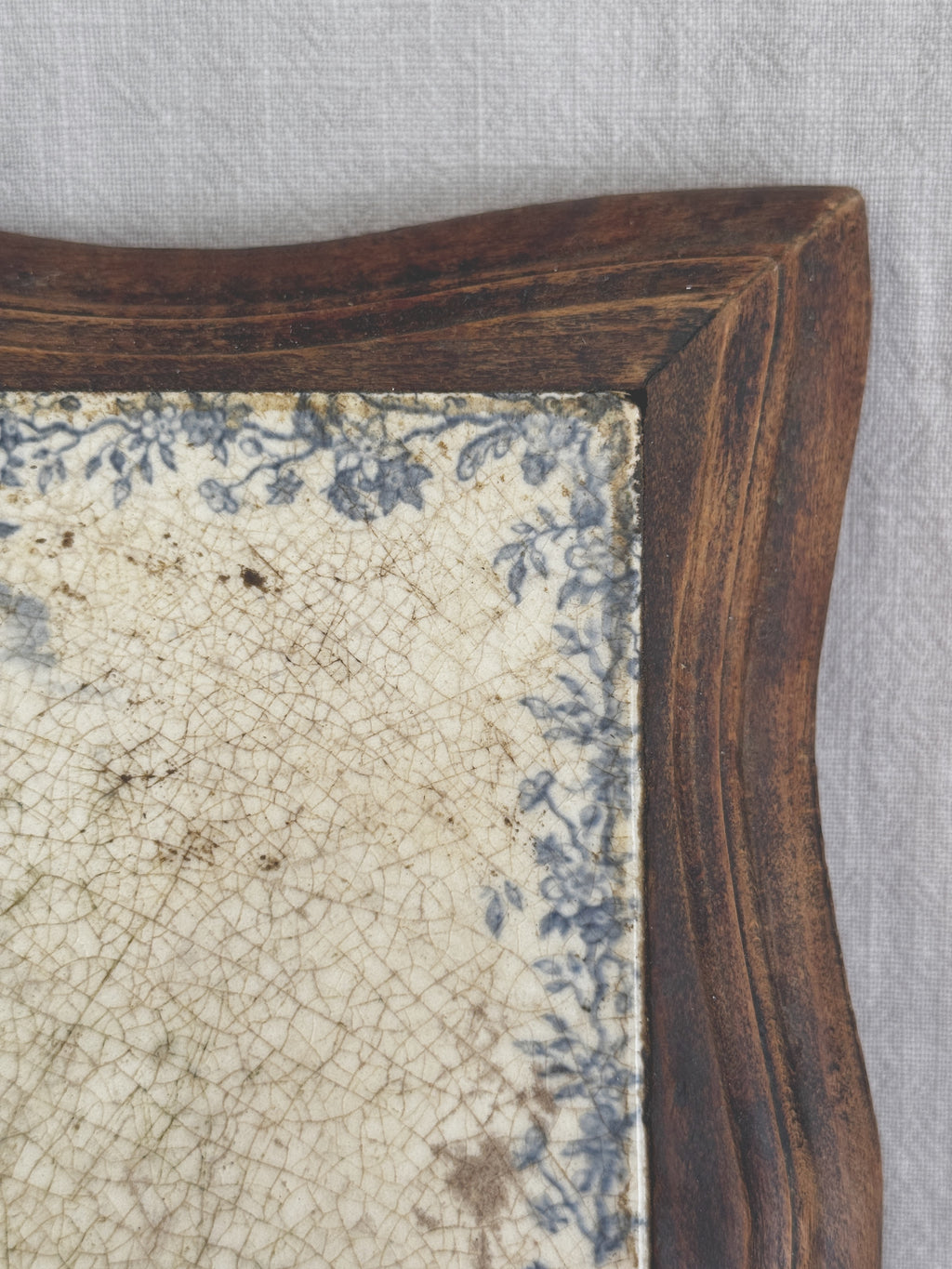Close-up of the upper corner of the tile, showing the floral border, brown age speckling and the wooden frame