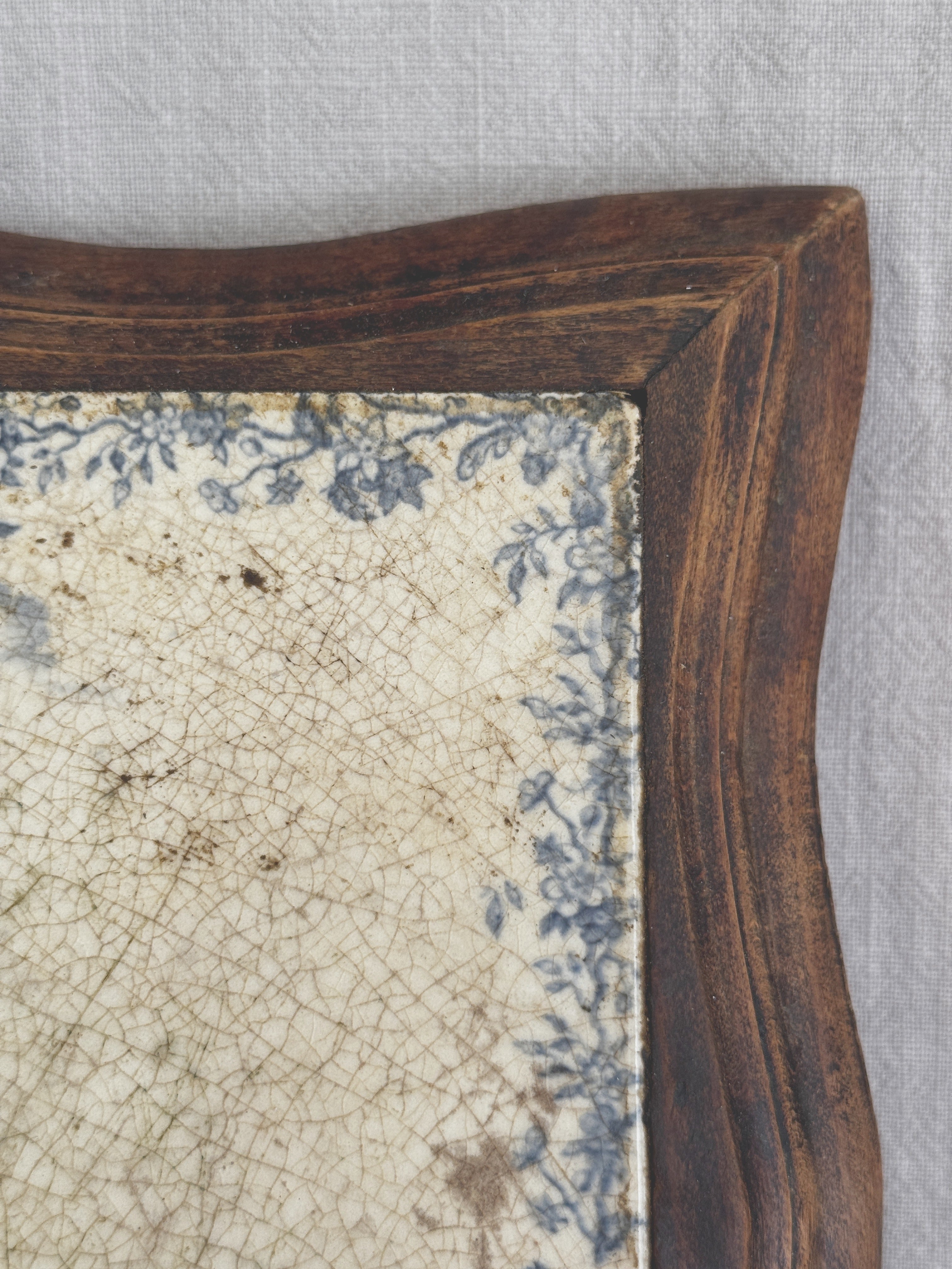 Close-up of the upper corner of the tile, showing the floral border, brown age speckling and the wooden frame