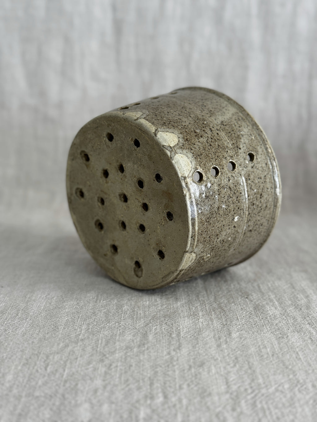 The stoneware cheese mould tipped on its side, showing the fully pierced base and pale glaze runs