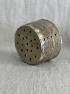 The stoneware cheese mould tipped on its side, showing the fully pierced base and pale glaze runs