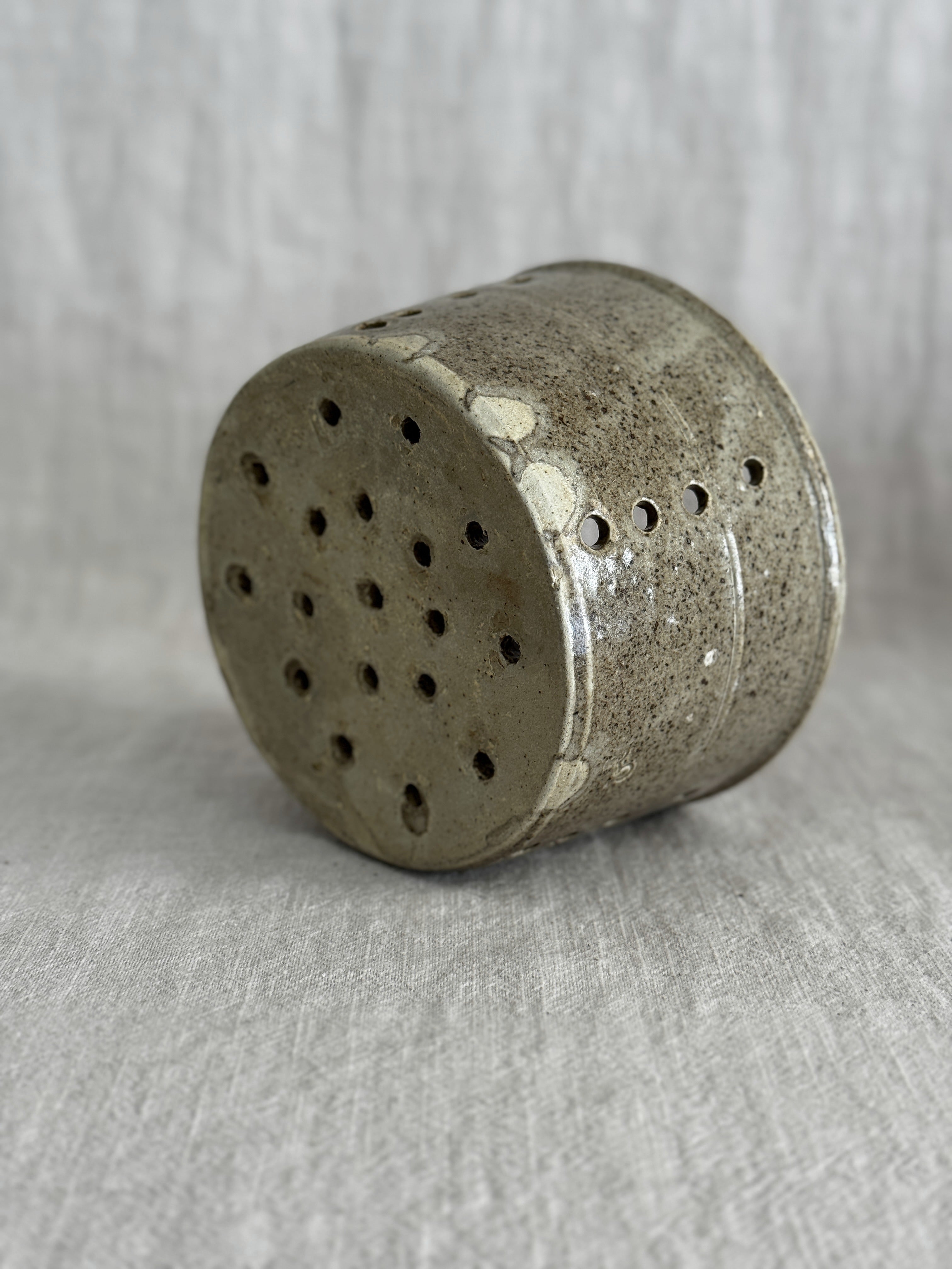 The stoneware cheese mould tipped on its side, showing the fully pierced base and pale glaze runs