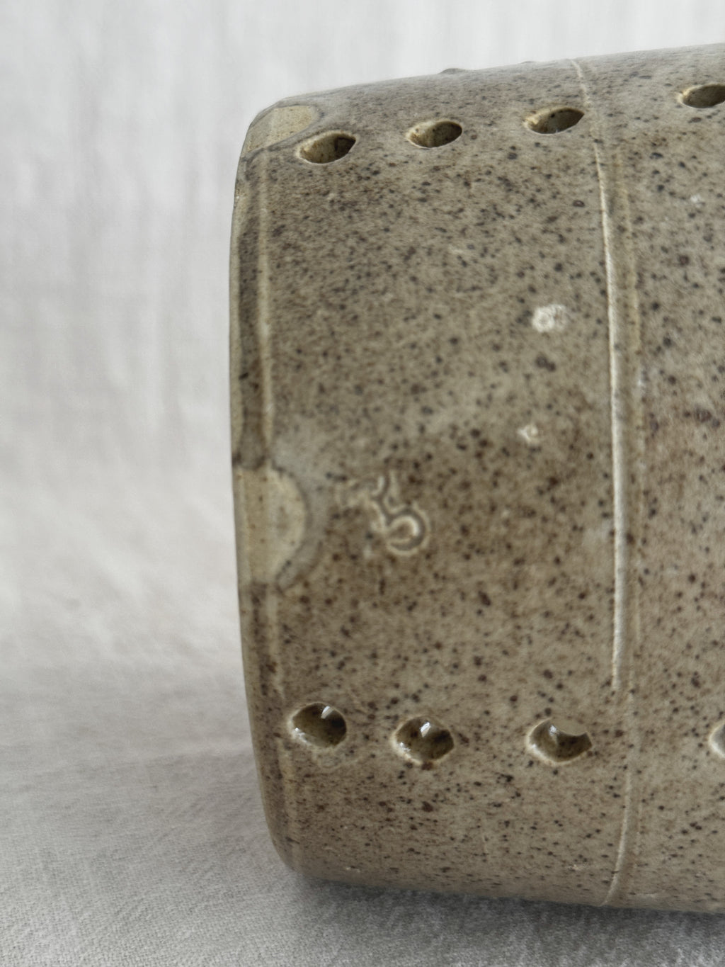 Close-up of the faisselle wall showing a small worn impressed mark, an incised turning line and drilled holes