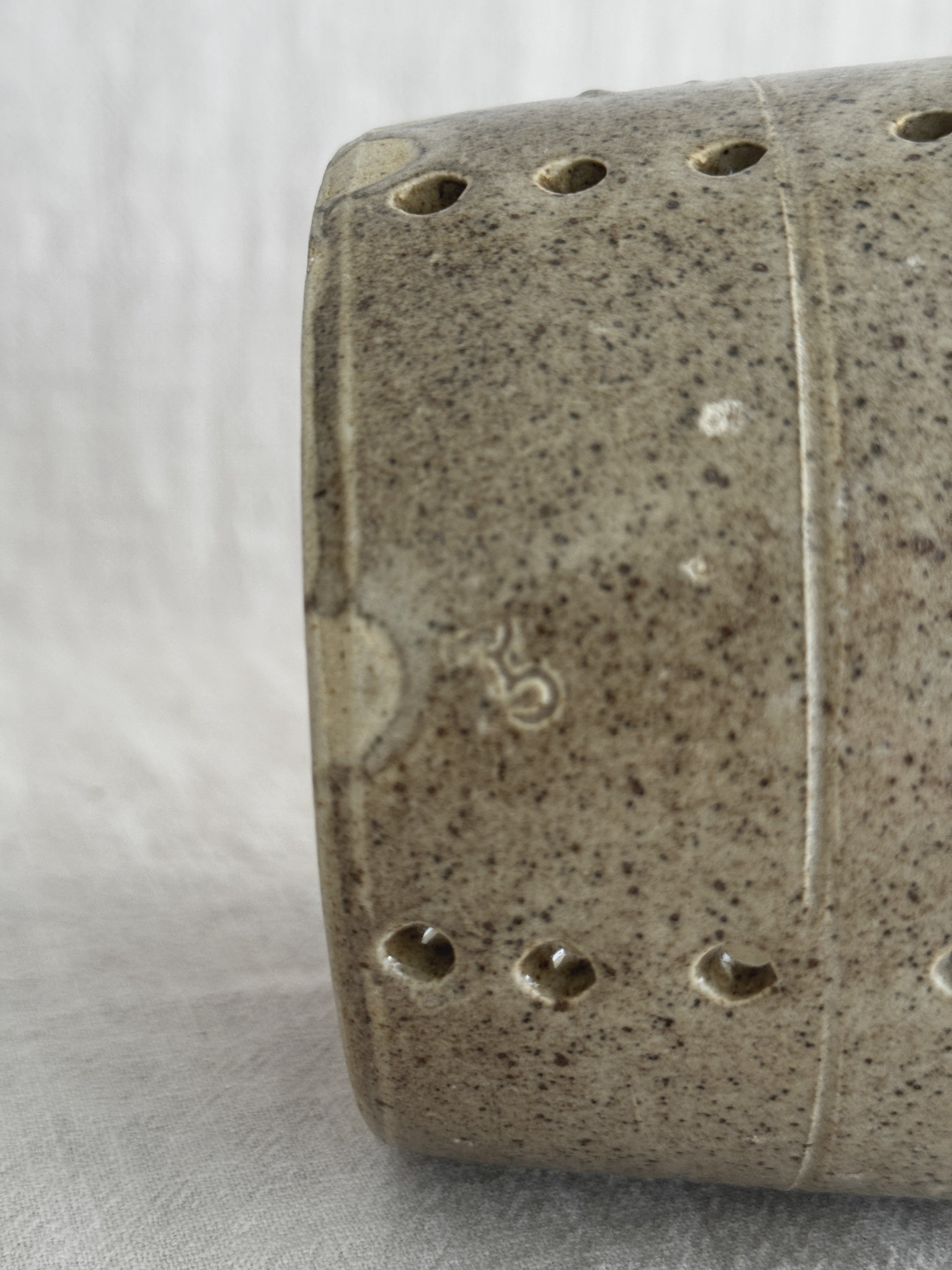 Close-up of the faisselle wall showing a small worn impressed mark, an incised turning line and drilled holes