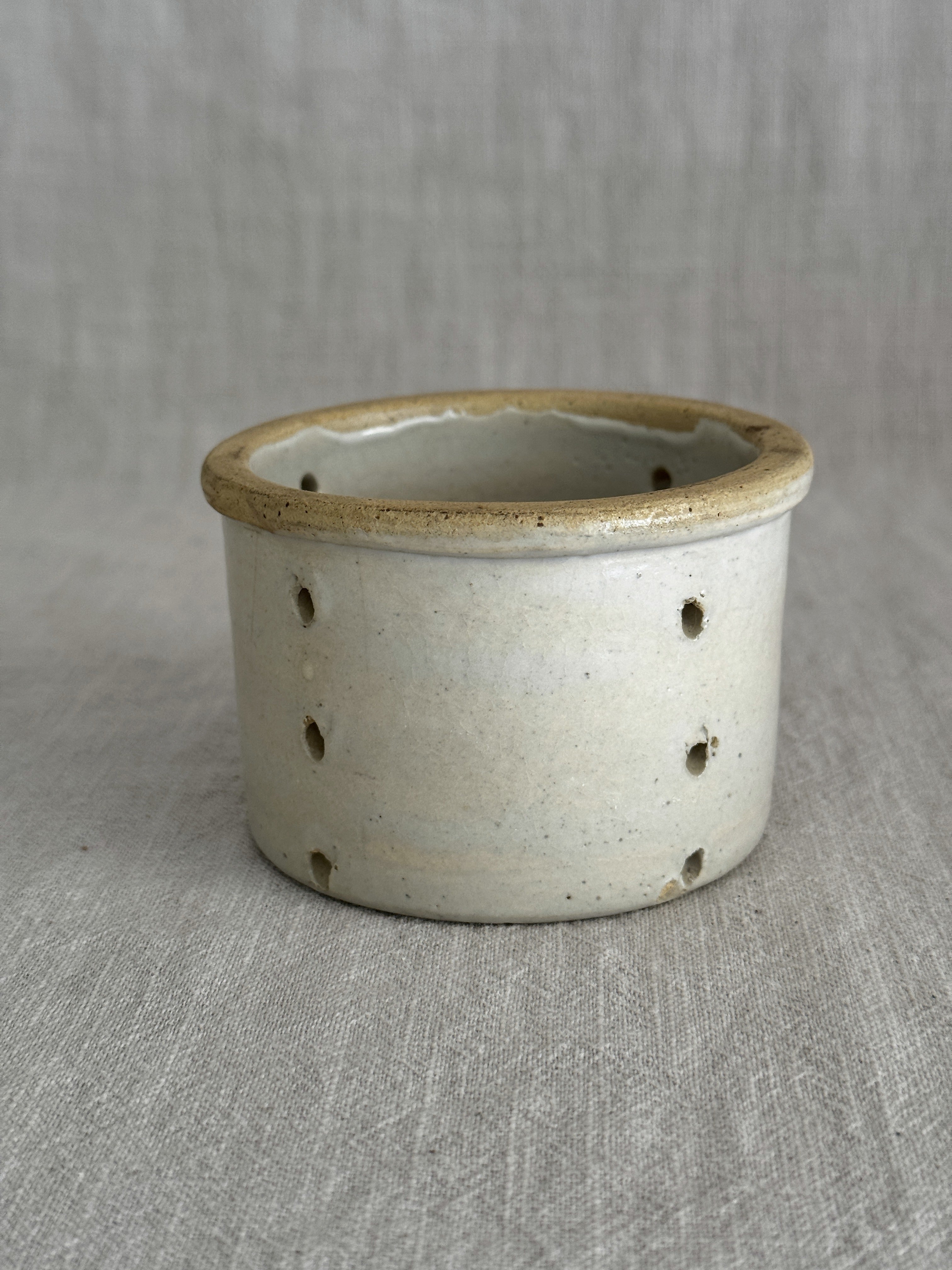 The smaller French faisselle, pale grey-cream stoneware with an ochre rolled rim and pierced walls