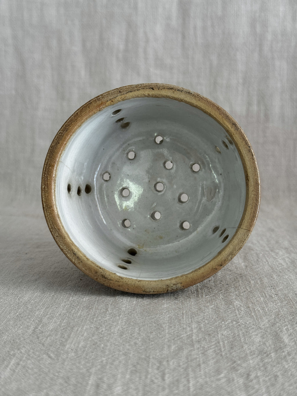 Side view of the larger cream-glazed faisselle showing the crazed glaze and hand-cut holes