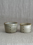 A pair of antique French faisselle cheese moulds in cream-glazed stoneware, standing side by side