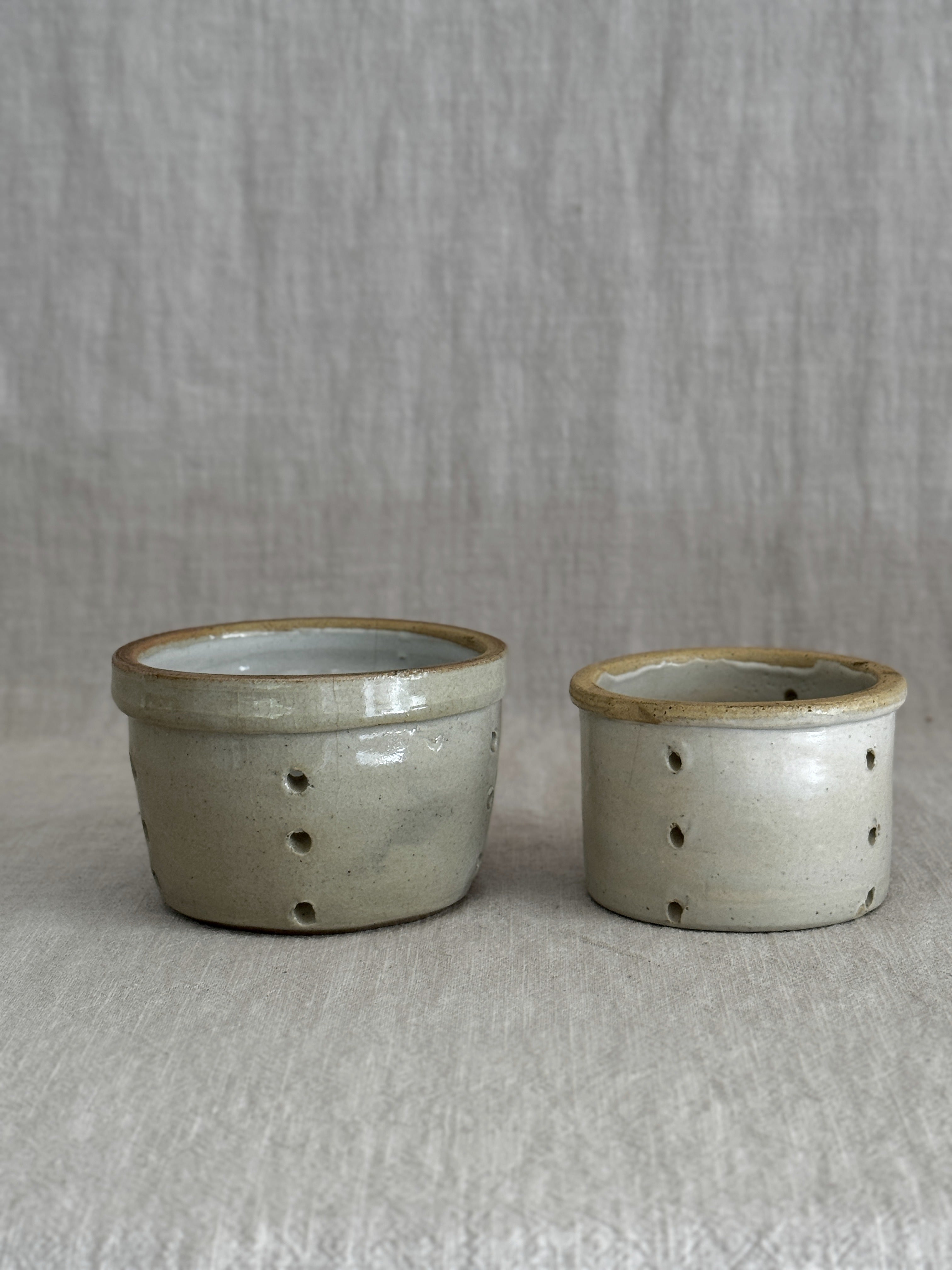 A pair of antique French faisselle cheese moulds in cream-glazed stoneware, standing side by side