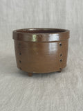 Brown salt-glazed French stoneware cheese mold standing upright on pale linen, two rows of pierced drain holes visible down the side