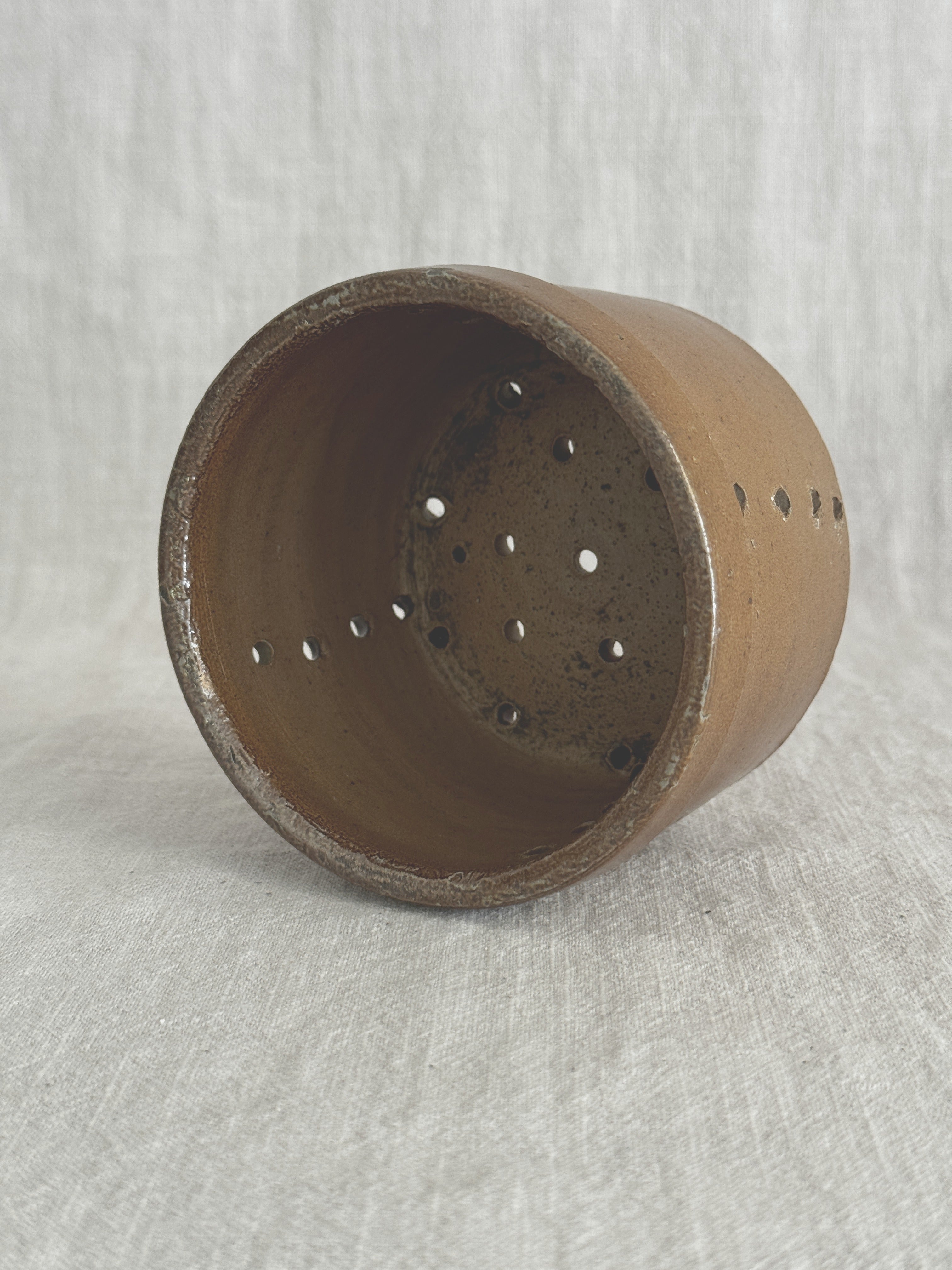 The same French faisselle tipped on its side, showing the glazed brown interior and the holes punched through the base