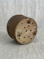 Underside of the stoneware cheese mold: unglazed buff clay base with a diamond pattern of drain holes and three small conical feet