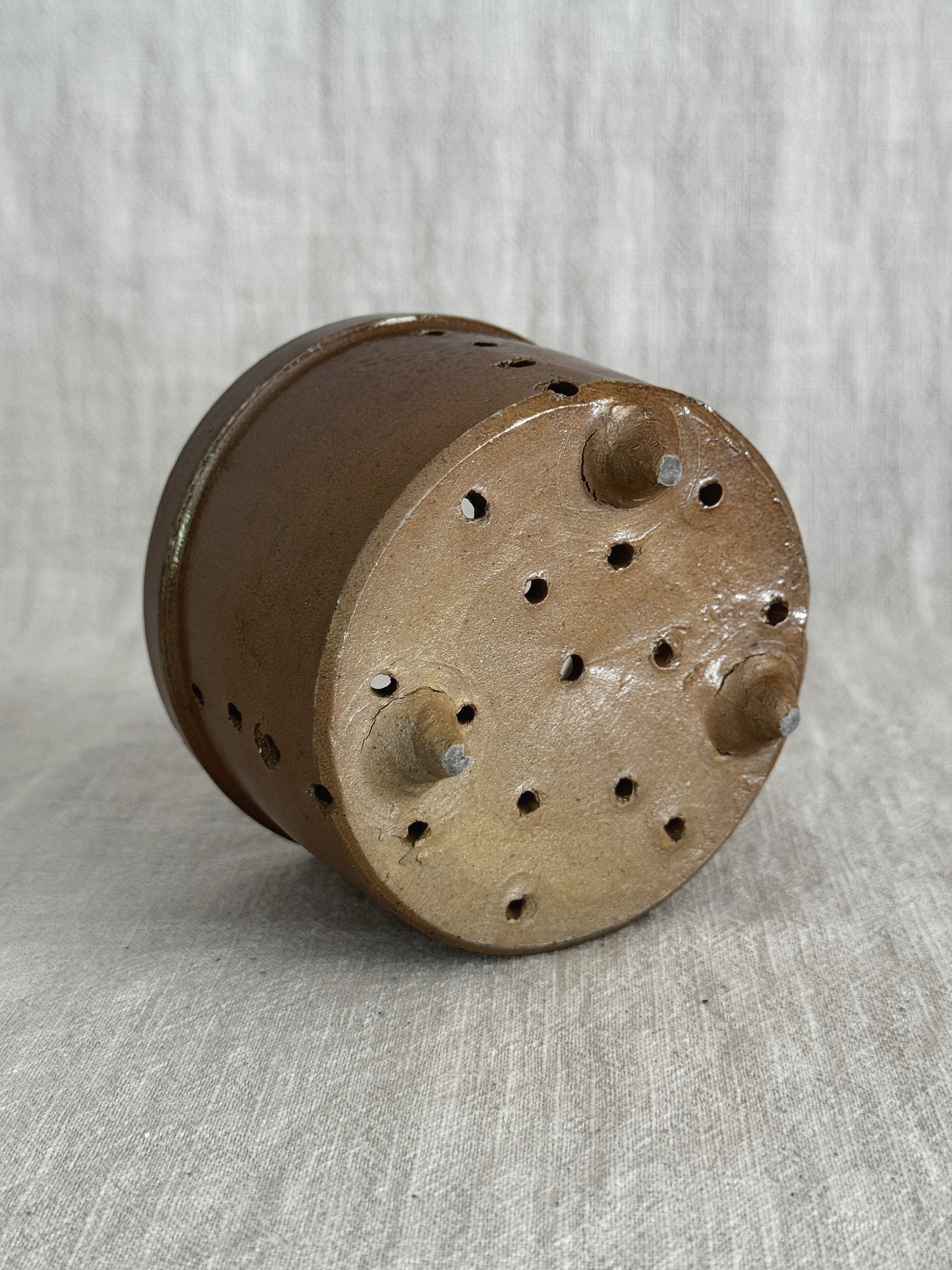 Underside of the stoneware cheese mold: unglazed buff clay base with a diamond pattern of drain holes and three small conical feet