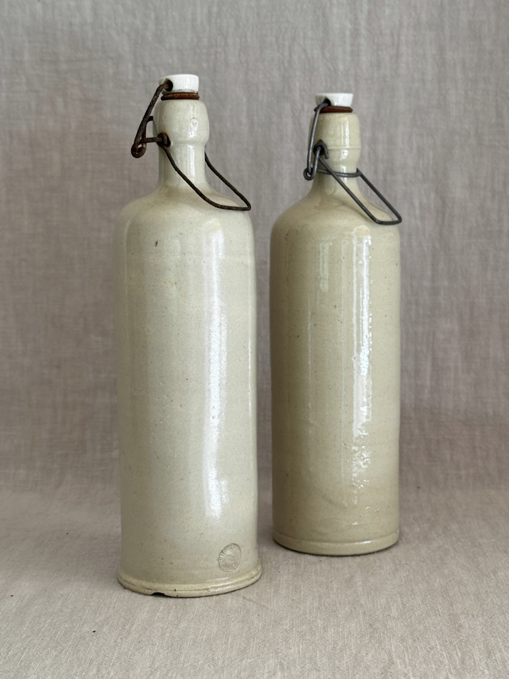 A pair of antique stoneware bail-top bottles with white porcelain stoppers, standing side by side