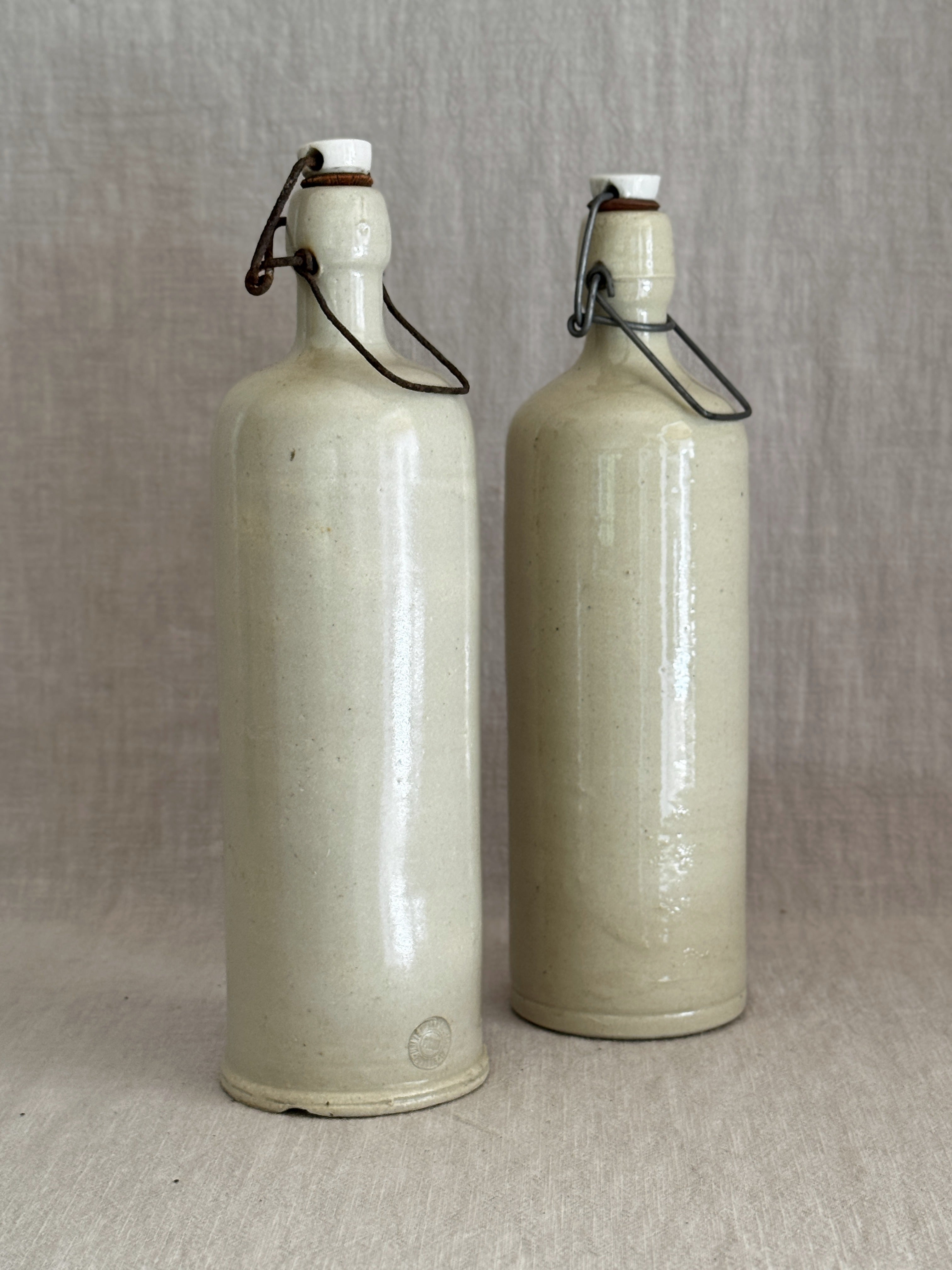 A pair of antique stoneware bail-top bottles with white porcelain stoppers, standing side by side