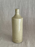 Unmarked French stoneware bottle in warm putty glaze standing on linen, the long fine glaze line running down the body