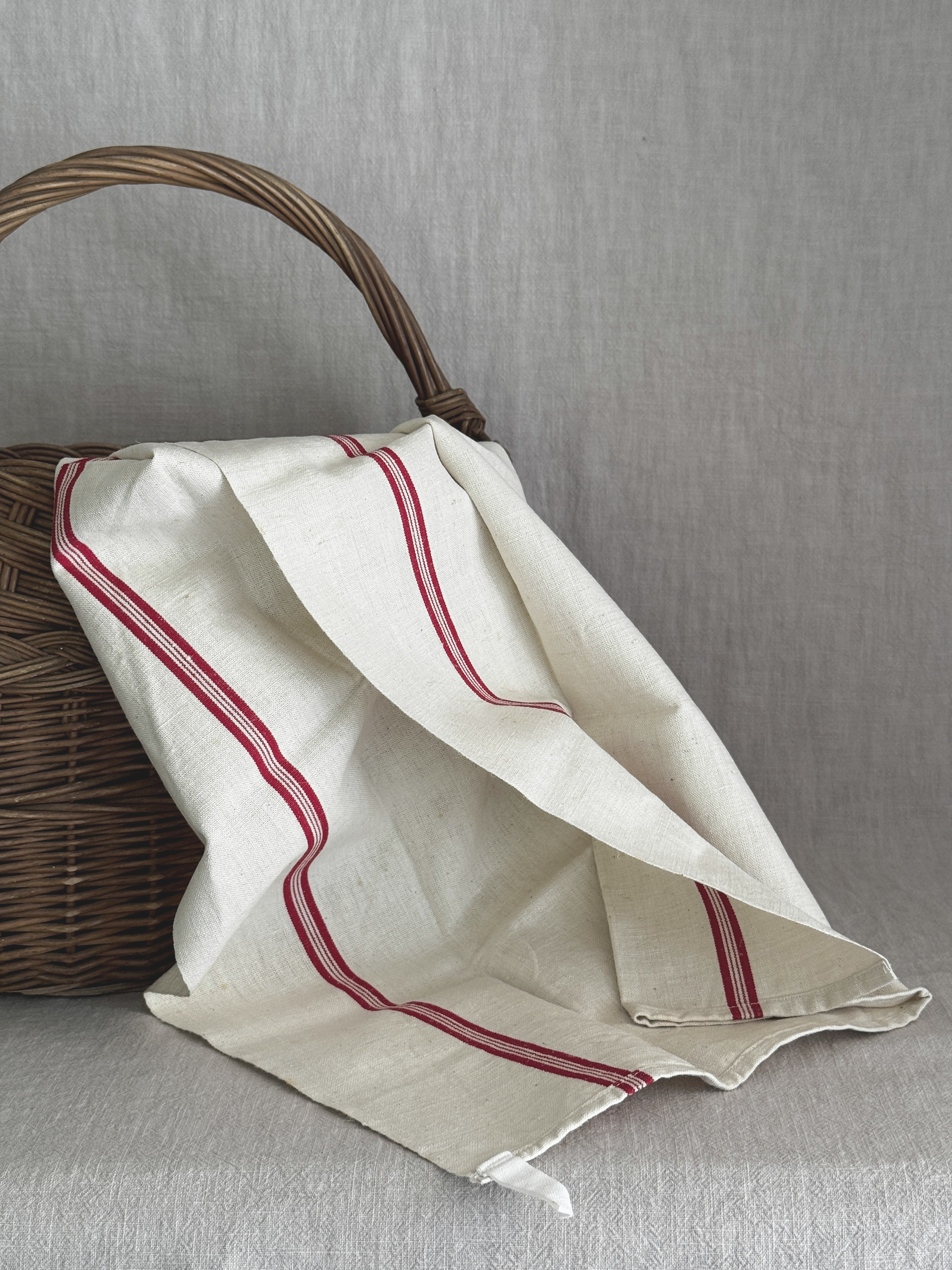 Cream linen torchon with red stripes draped over an old wicker basket against a grey linen backdrop