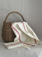 Red-striped French linen torchon draped over a woven basket with a second folded towel beside it