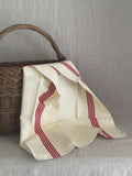 Unused cream French toile metis torchon with red stripes draped over an old wicker basket, printed selvedge mark visible at the corner