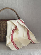 Unused cream French toile metis torchon with red stripes draped over an old wicker basket, printed selvedge mark visible at the corner