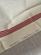 Blue printed selvedge mark reading TOILE METIS Fleur Bleue 127 beside the red woven stripes on cream metis cloth