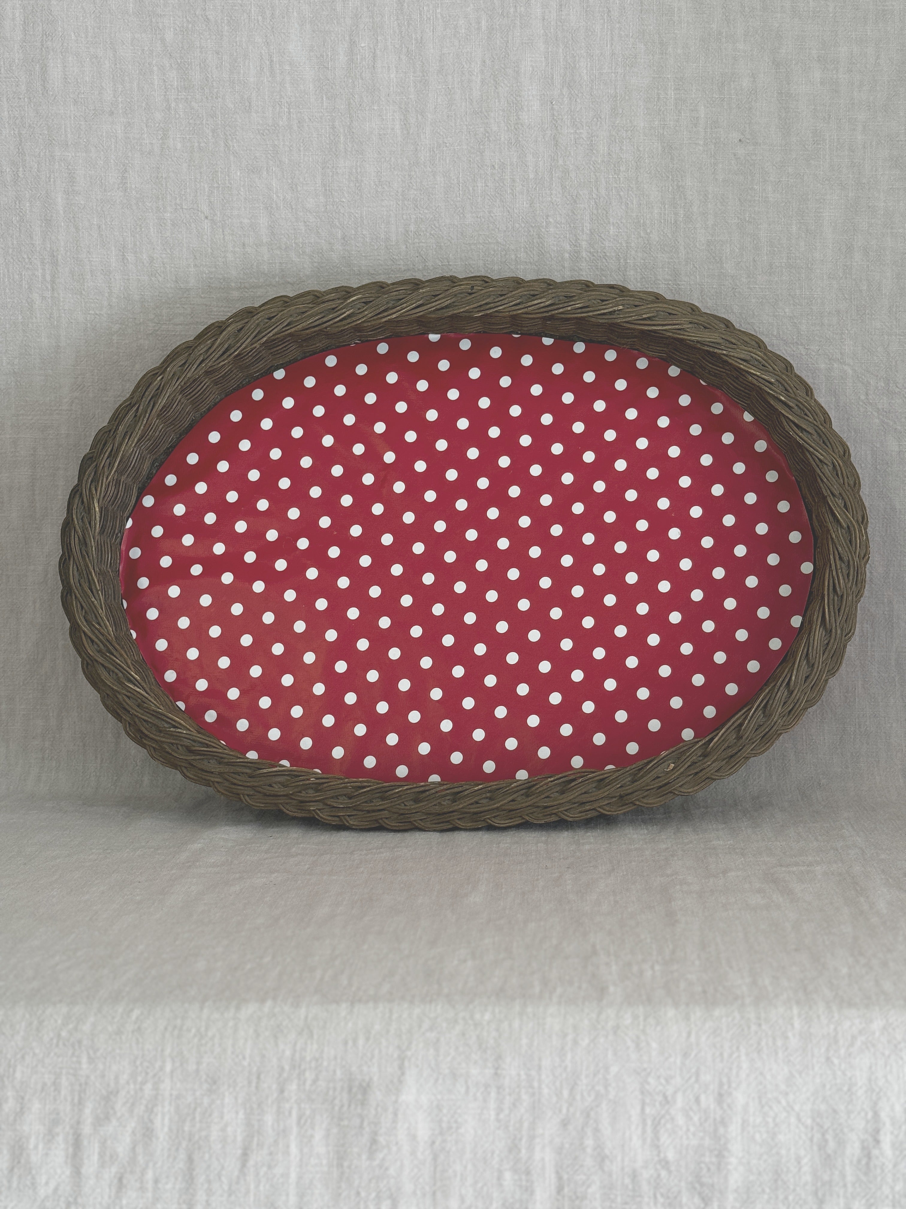 Large oval willow basket tray seen from above, lined with red and white polka dot oilcloth, on a linen cloth