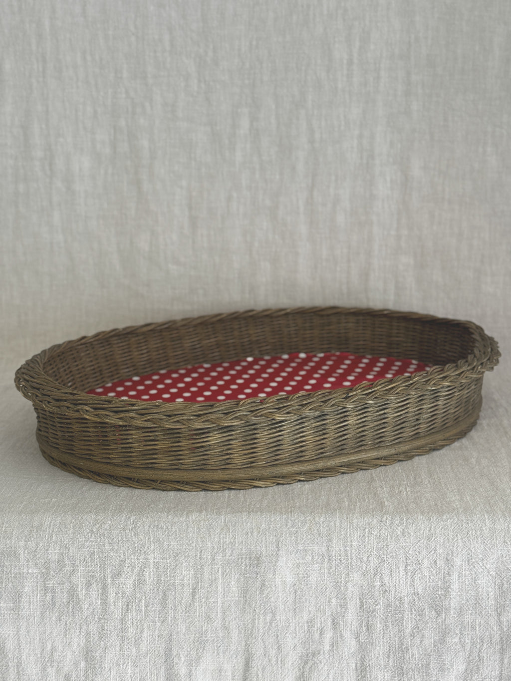 Oval wicker basket tray photographed from the side, showing the deep plaited sides and the red dotted base inside