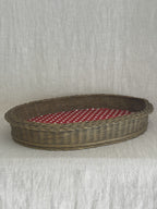 Oval wicker basket tray photographed from the side, showing the deep plaited sides and the red dotted base inside