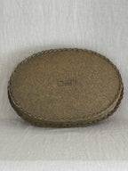 Underside of the oval willow tray showing the plain fibreboard base, the plaited edge and the maker's stamp