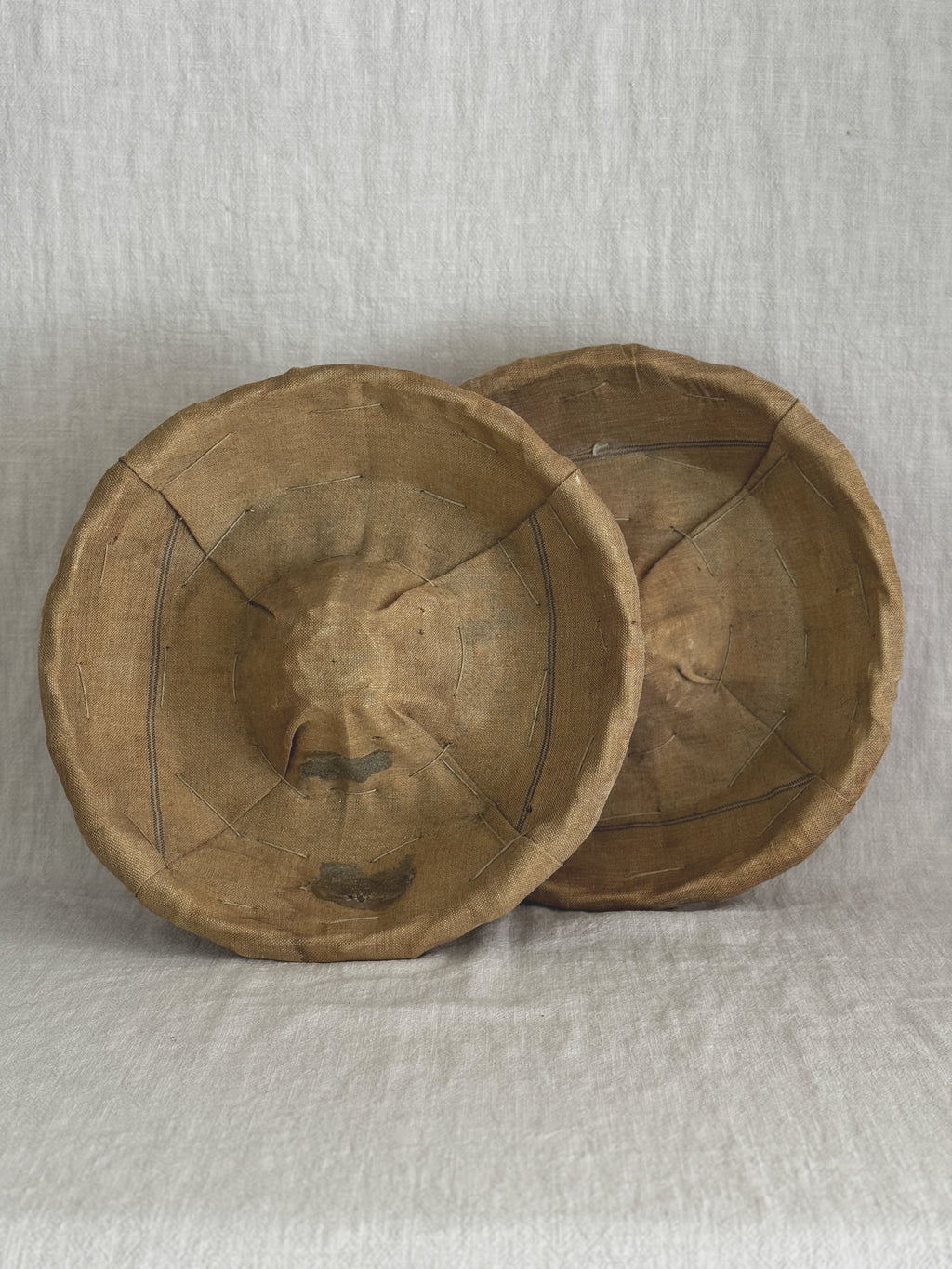 Two vintage French bannetons standing upright, showing the flour-patinated striped linen liners inside