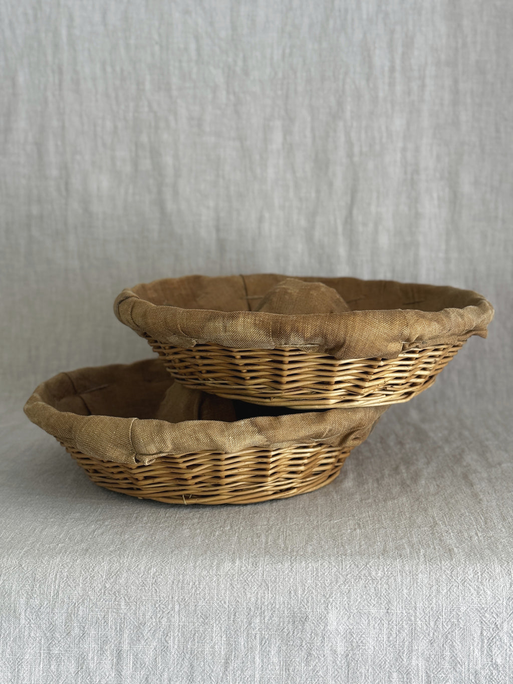 Two round willow bread proofing baskets stacked at an angle, linen liners folded over the woven rims
