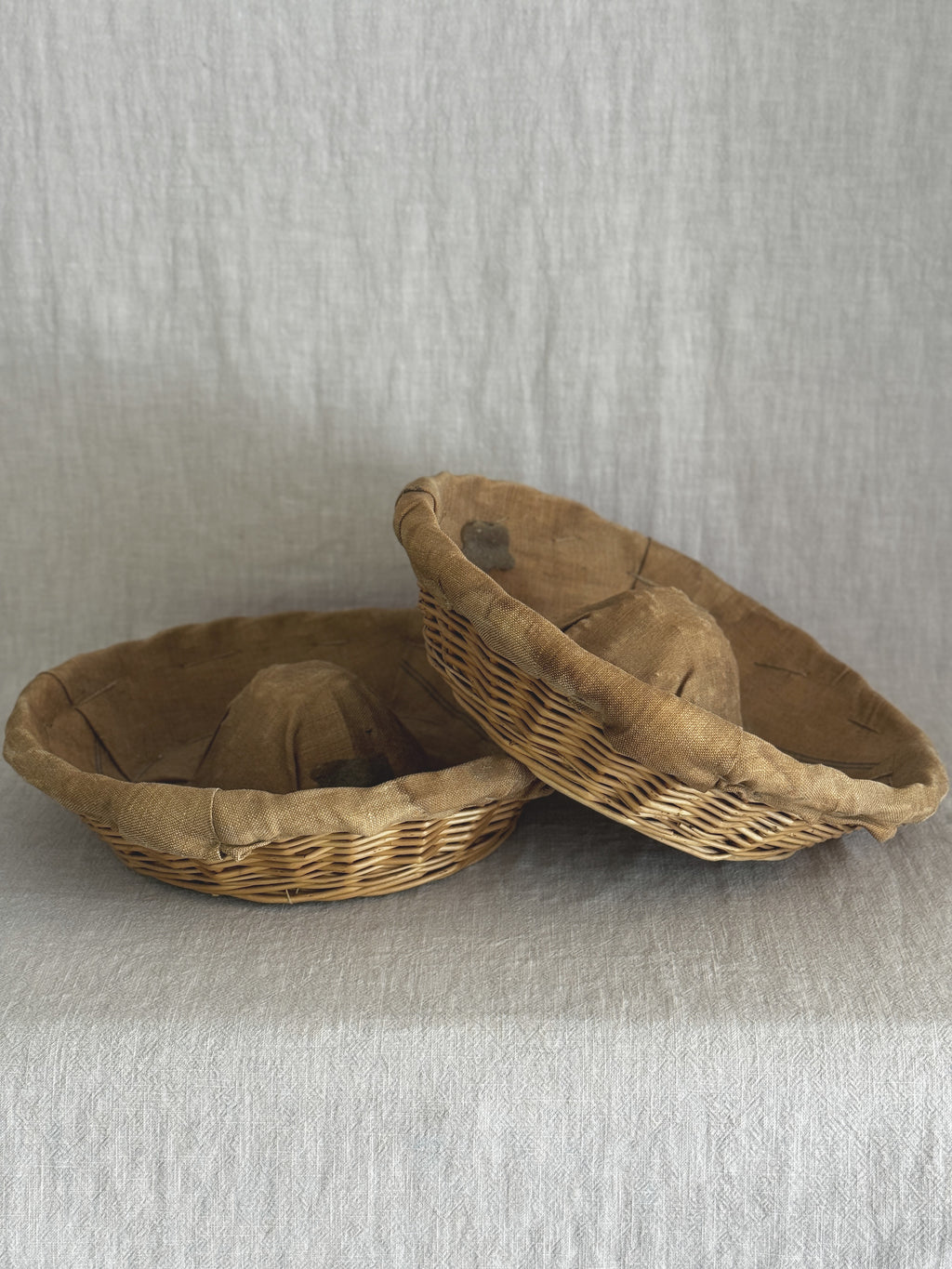 Pair of French banneton baskets side by side on a linen backdrop, one tipped to show the lining