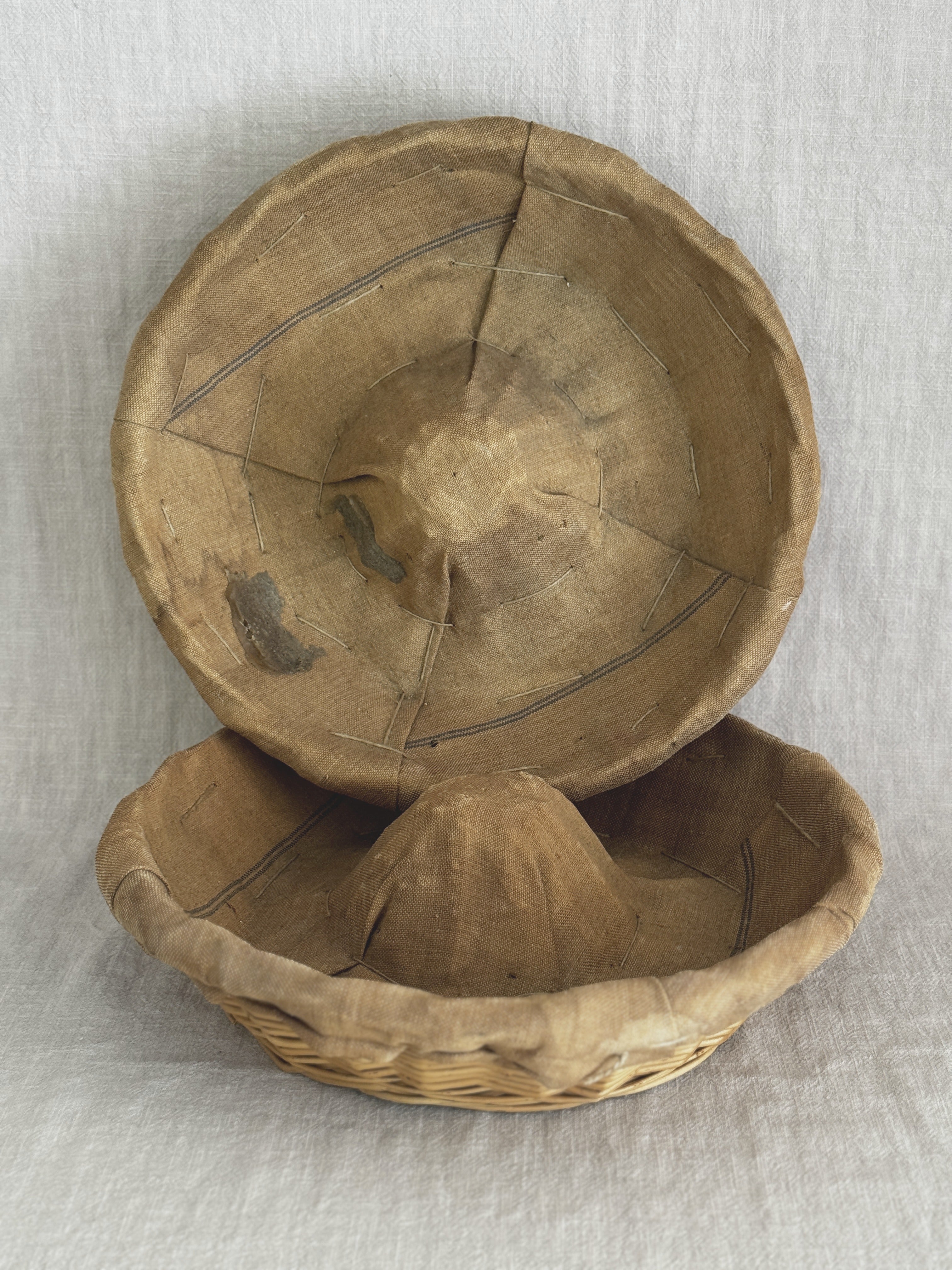 Two linen-lined bannetons, one propped upright, showing the staining and soft creases in the aged liner