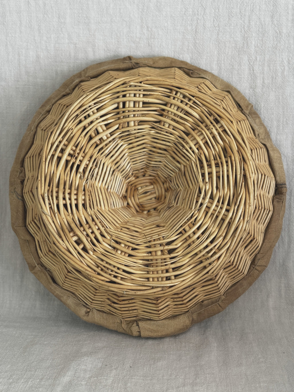 Underside of a round French banneton showing the spiral-woven willow base and the linen edge