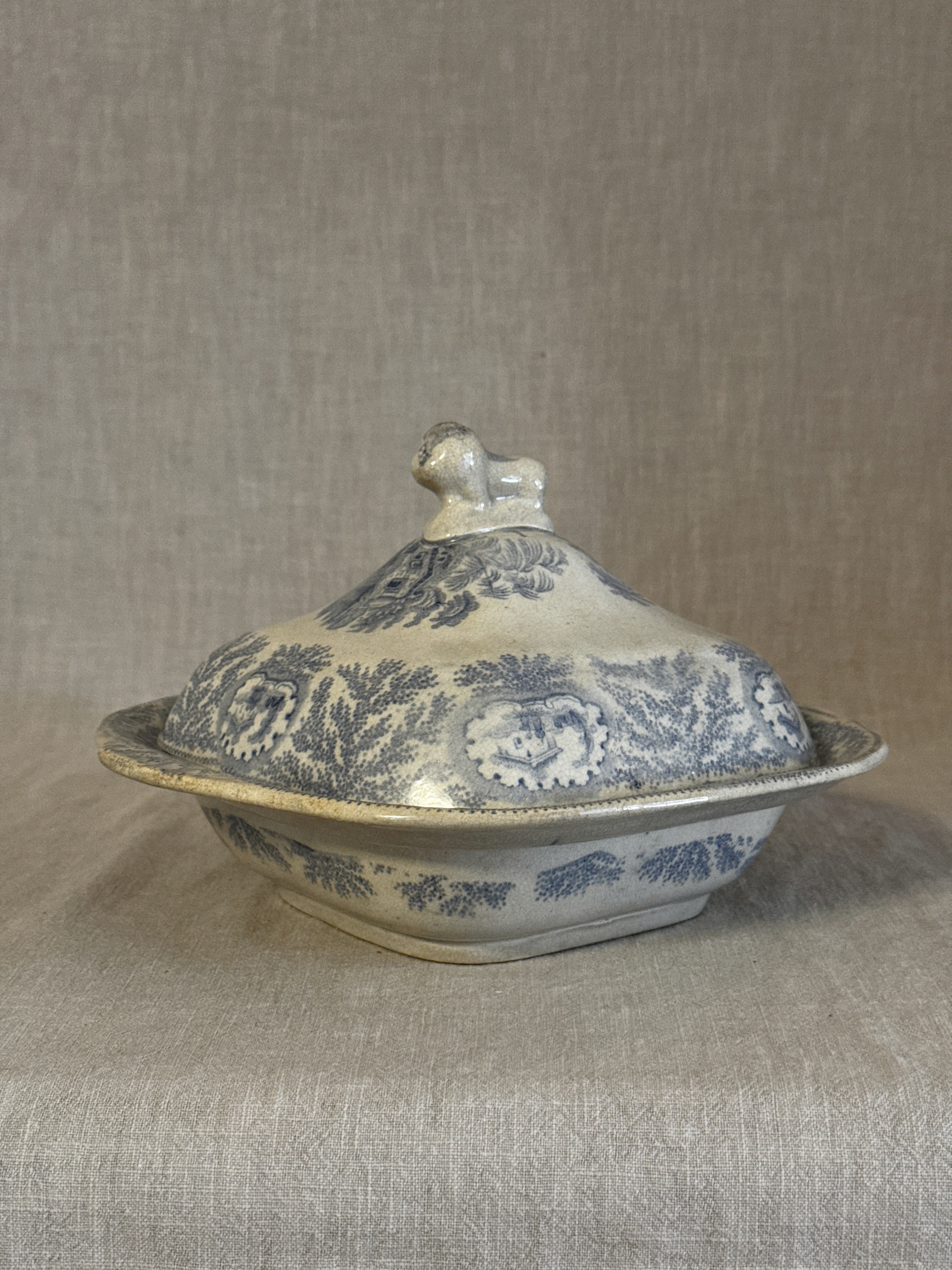 Side view of the blue transferware covered dish showing the lid, lion finial and pastoral pattern