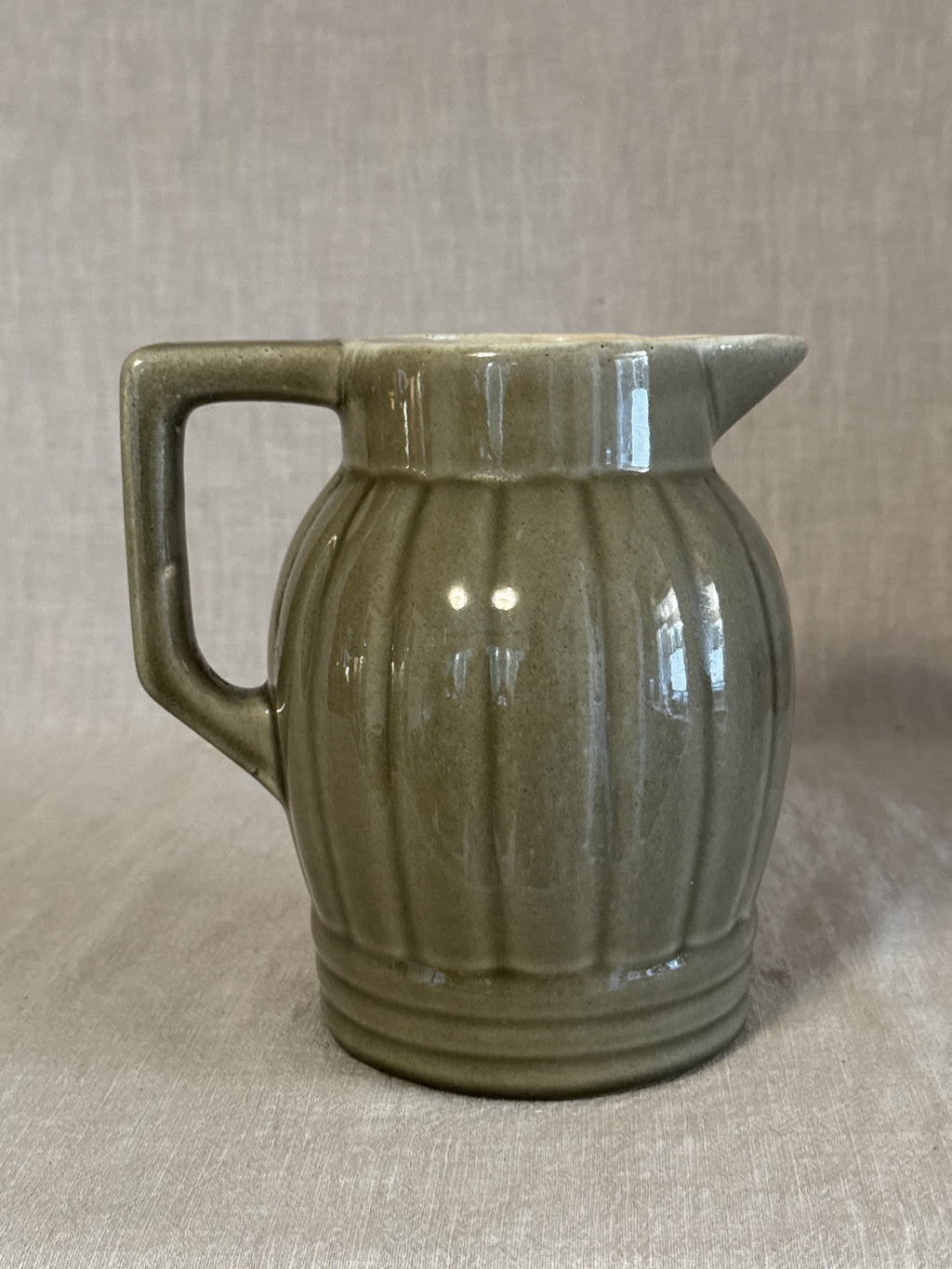 Side view of the olive green ribbed jug showing the vertical ribbing