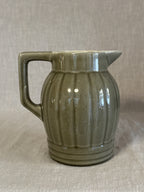 Side view of the olive green ribbed jug showing the vertical ribbing