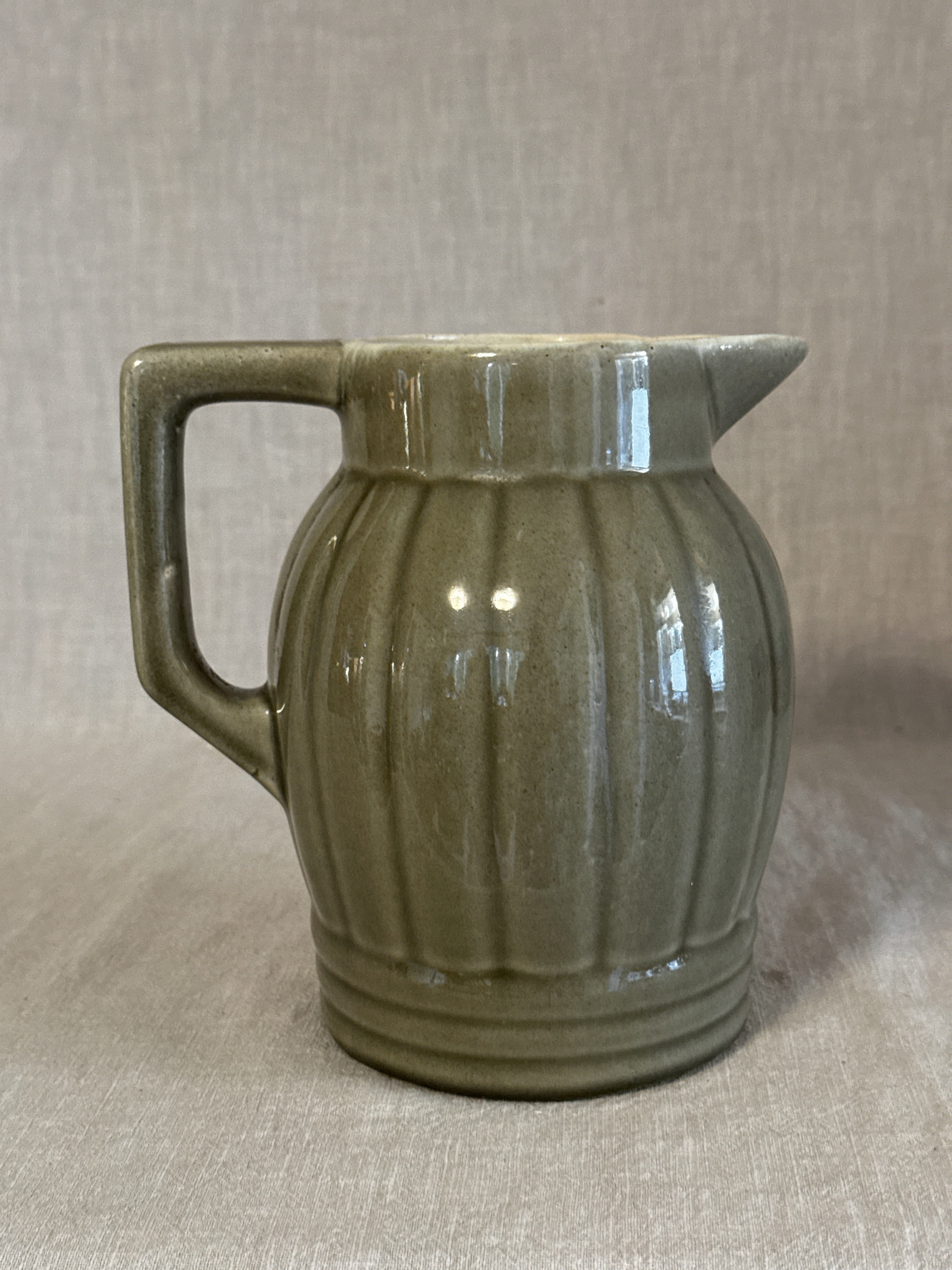 Side view of the olive green ribbed jug showing the vertical ribbing