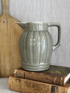 Vintage ribbed olive green glazed jug shown on antique books beside a bread board for size reference