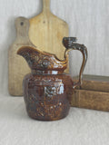 Antique treacle-glazed relief jug with a horse's head handle, styled with a bread board and old books