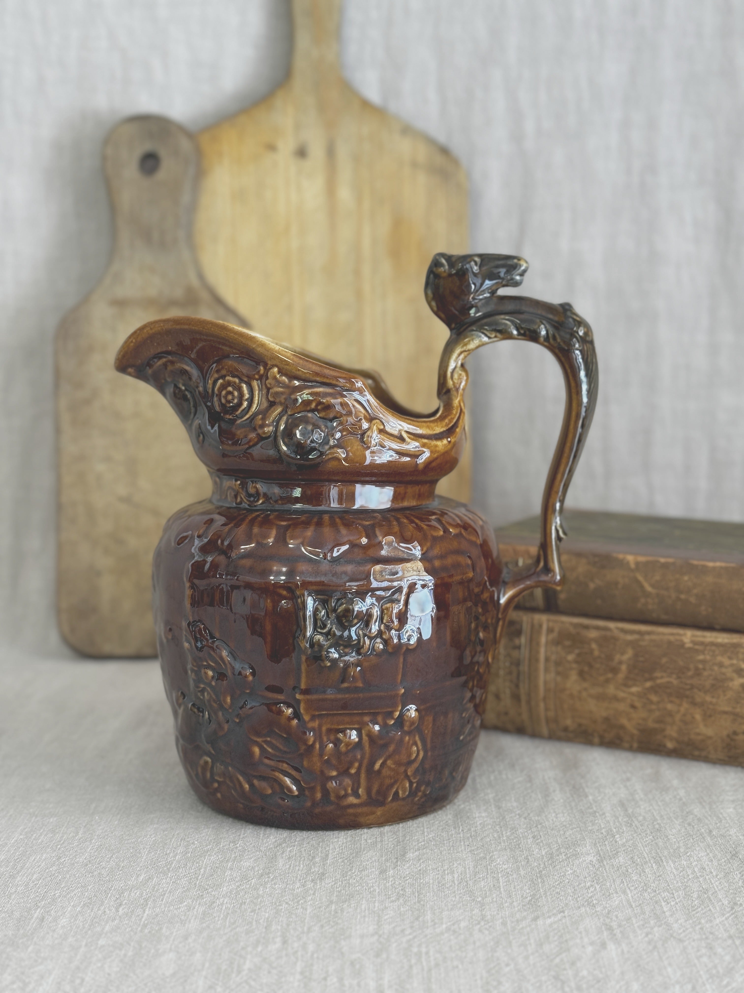 Antique treacle-glazed relief jug with a horse's head handle, styled with a bread board and old books