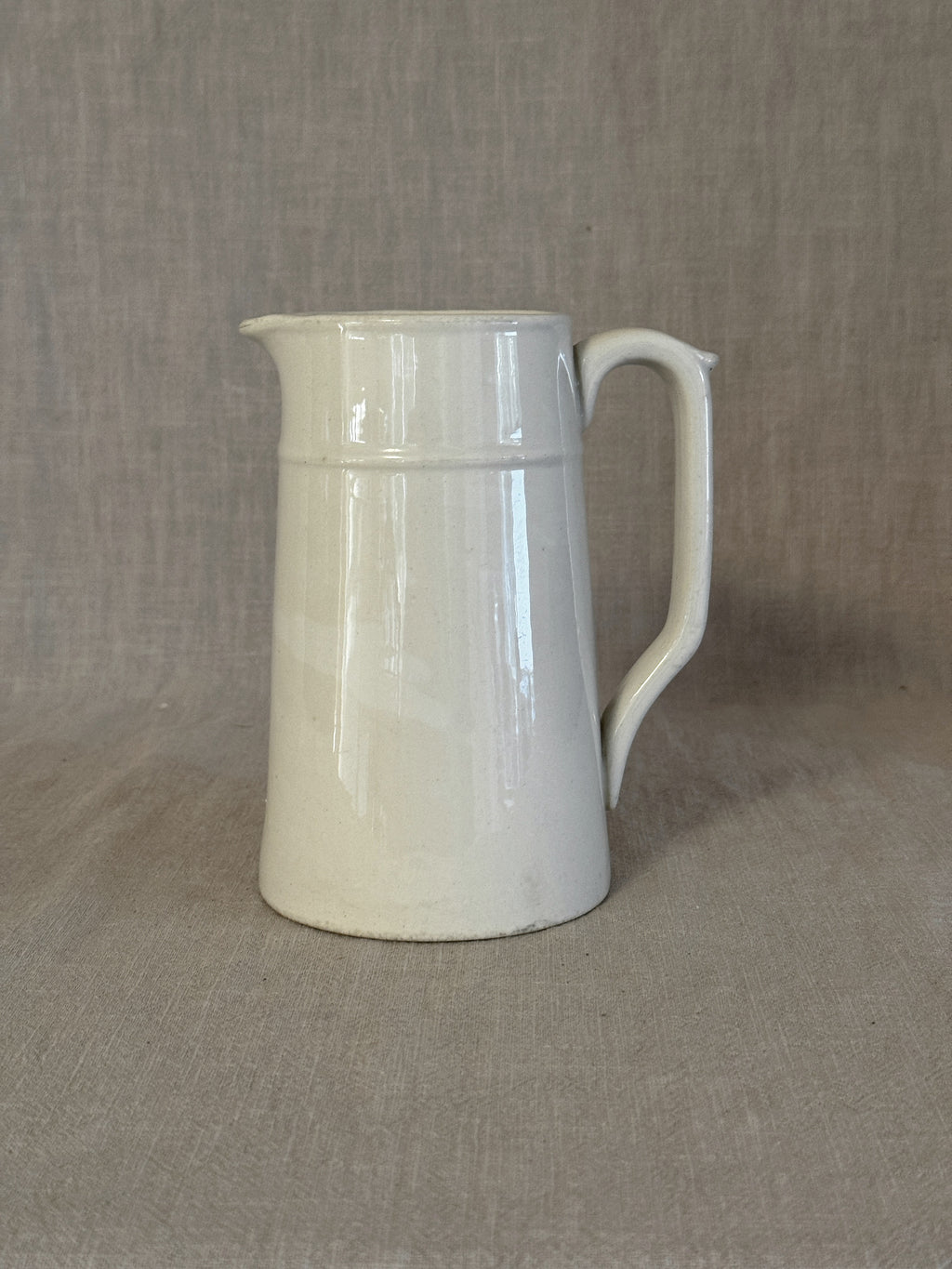 Small plain white Swedish jug in white earthenware with a strap handle, on linen