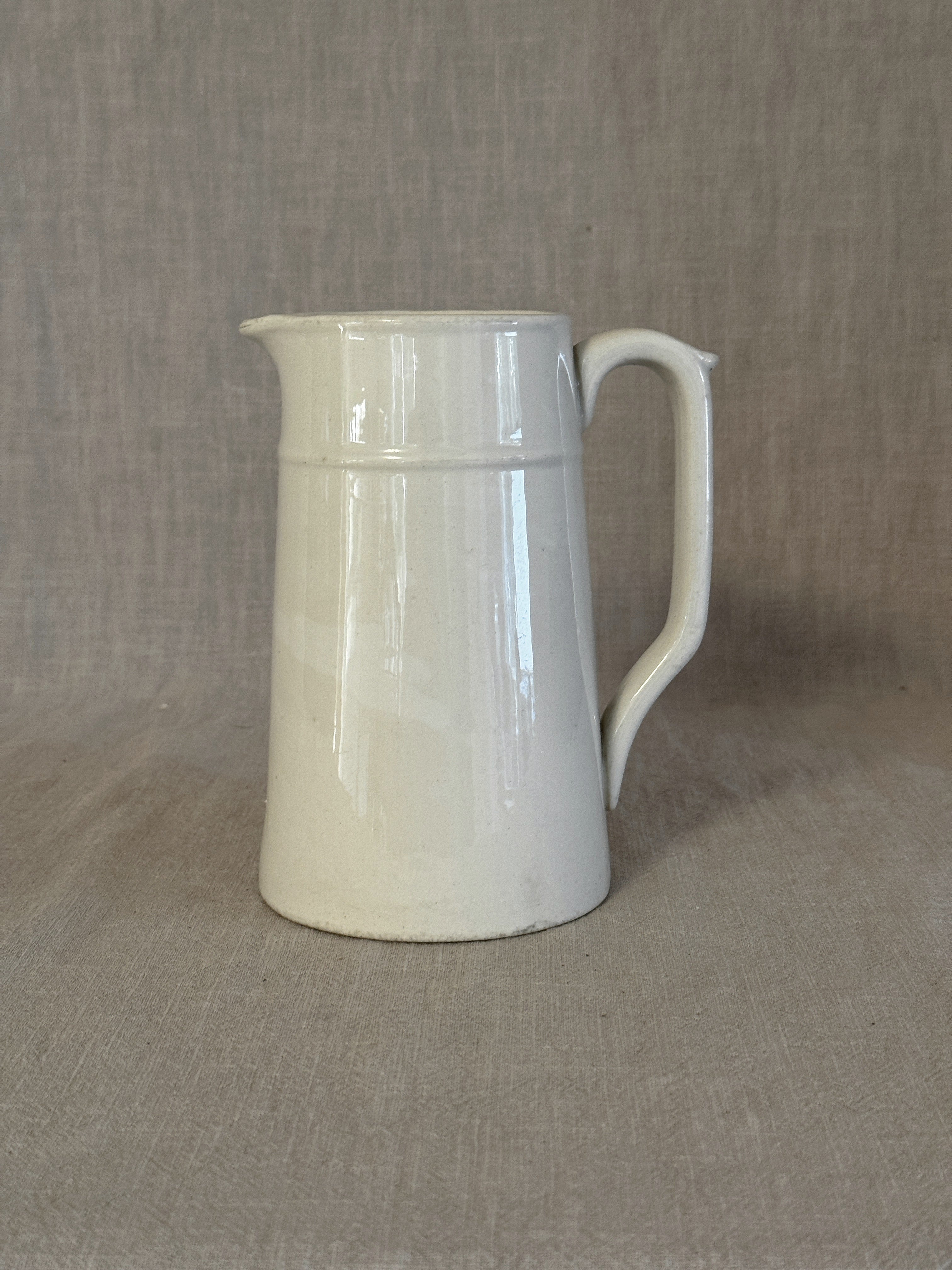 Small plain white Swedish jug in white earthenware with a strap handle, on linen