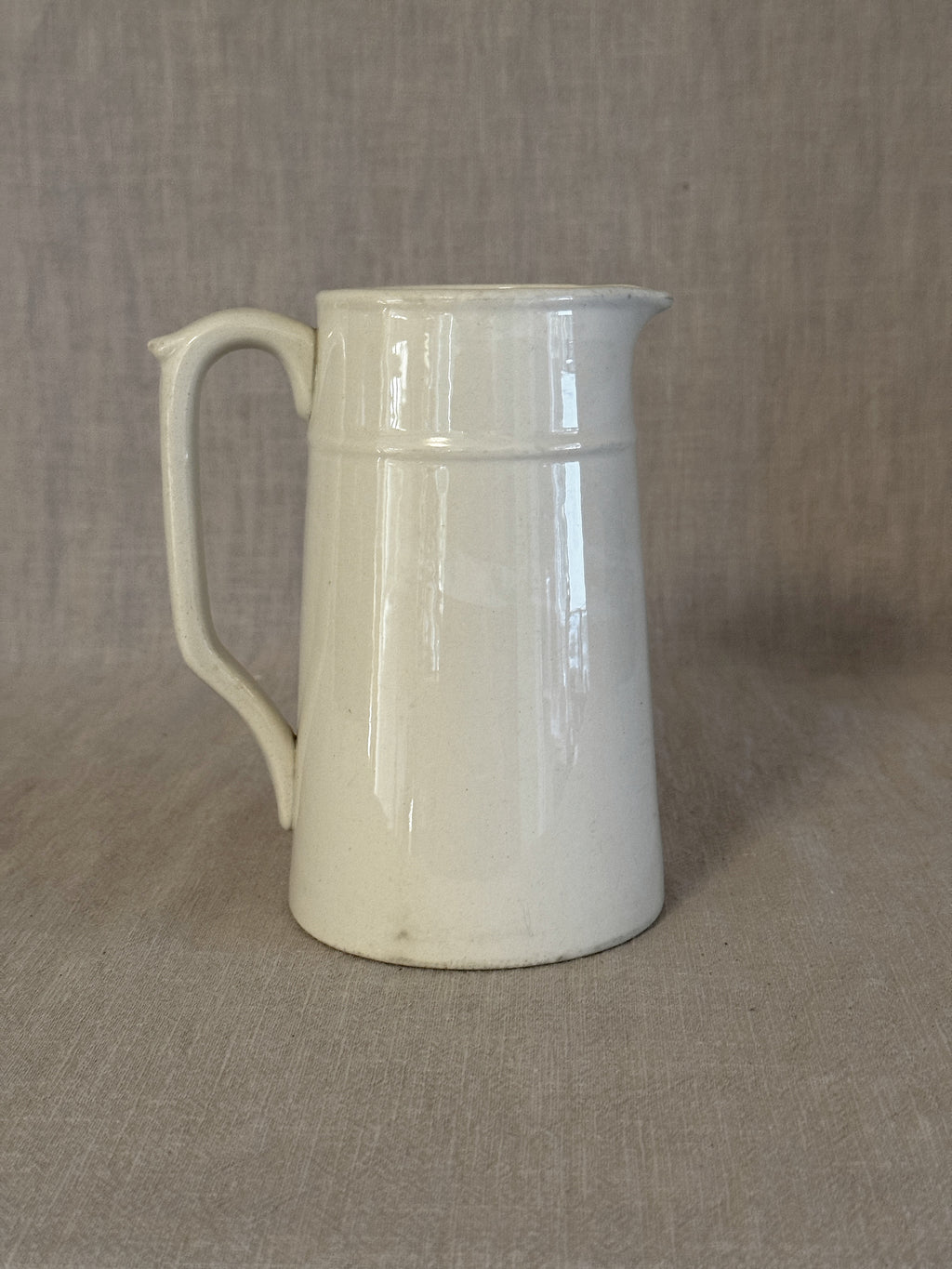 Side view of the small white earthenware jug showing its straight tapered form