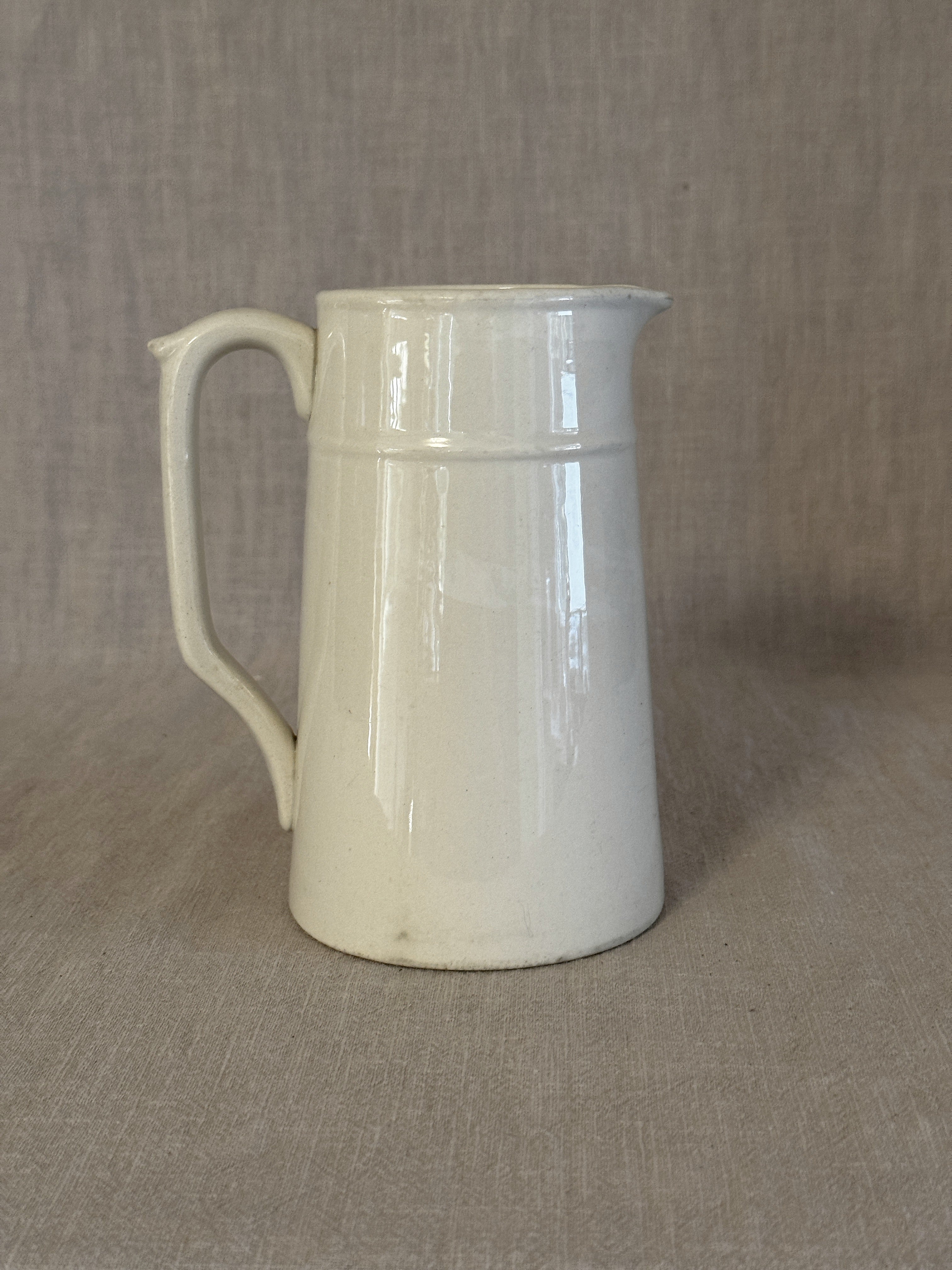 Side view of the small white earthenware jug showing its straight tapered form