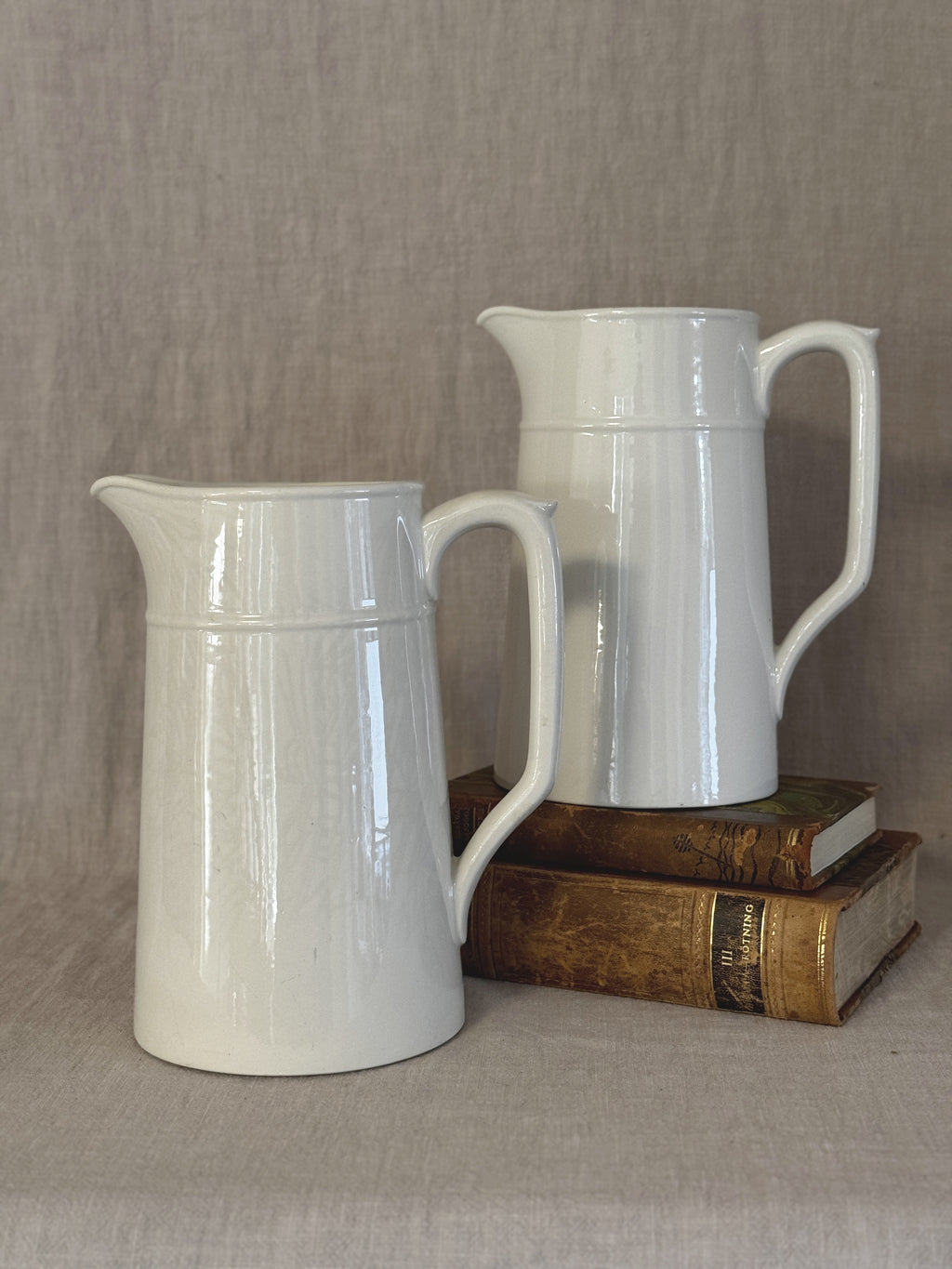 Two matching tall white Swedish jugs in plain white earthenware, styled with old books