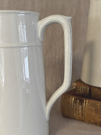 Close view of one tall white jug showing the strap handle and raised neck band