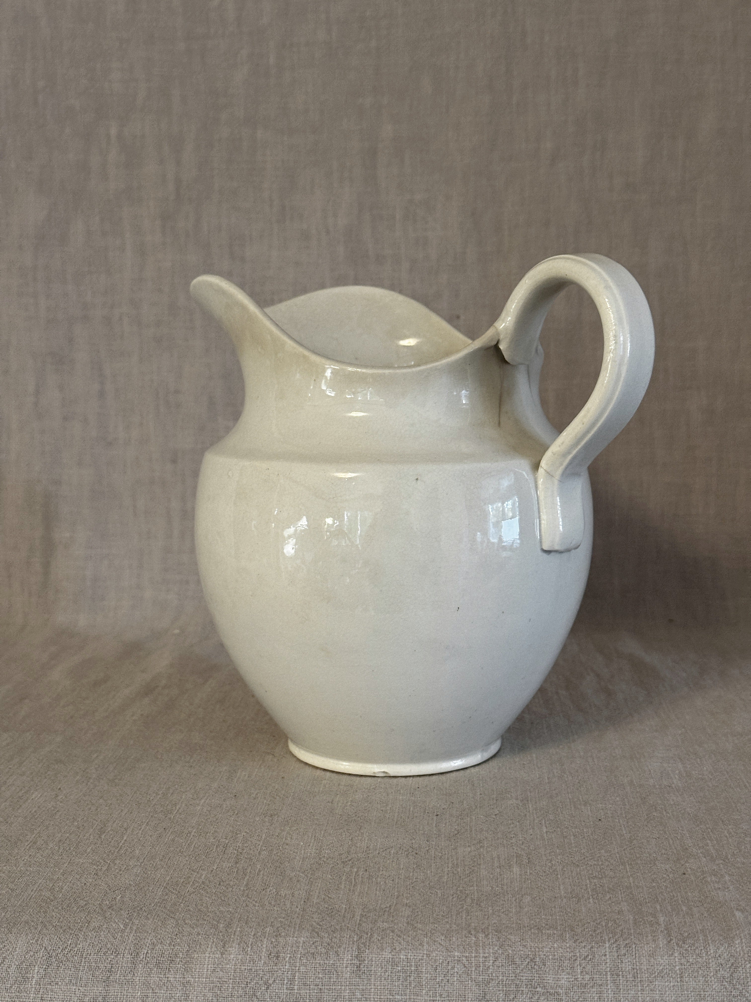 Side view of the white washstand jug showing its rounded body and warm patina